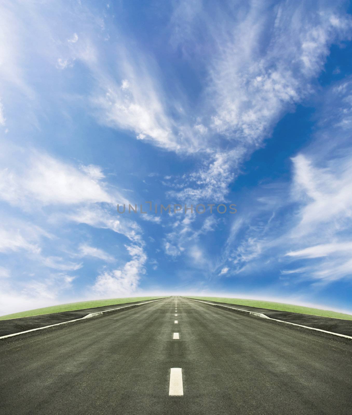 Shot of a tarmac road leading into the horizon. Beautiful blue sky and green slope beneath it.