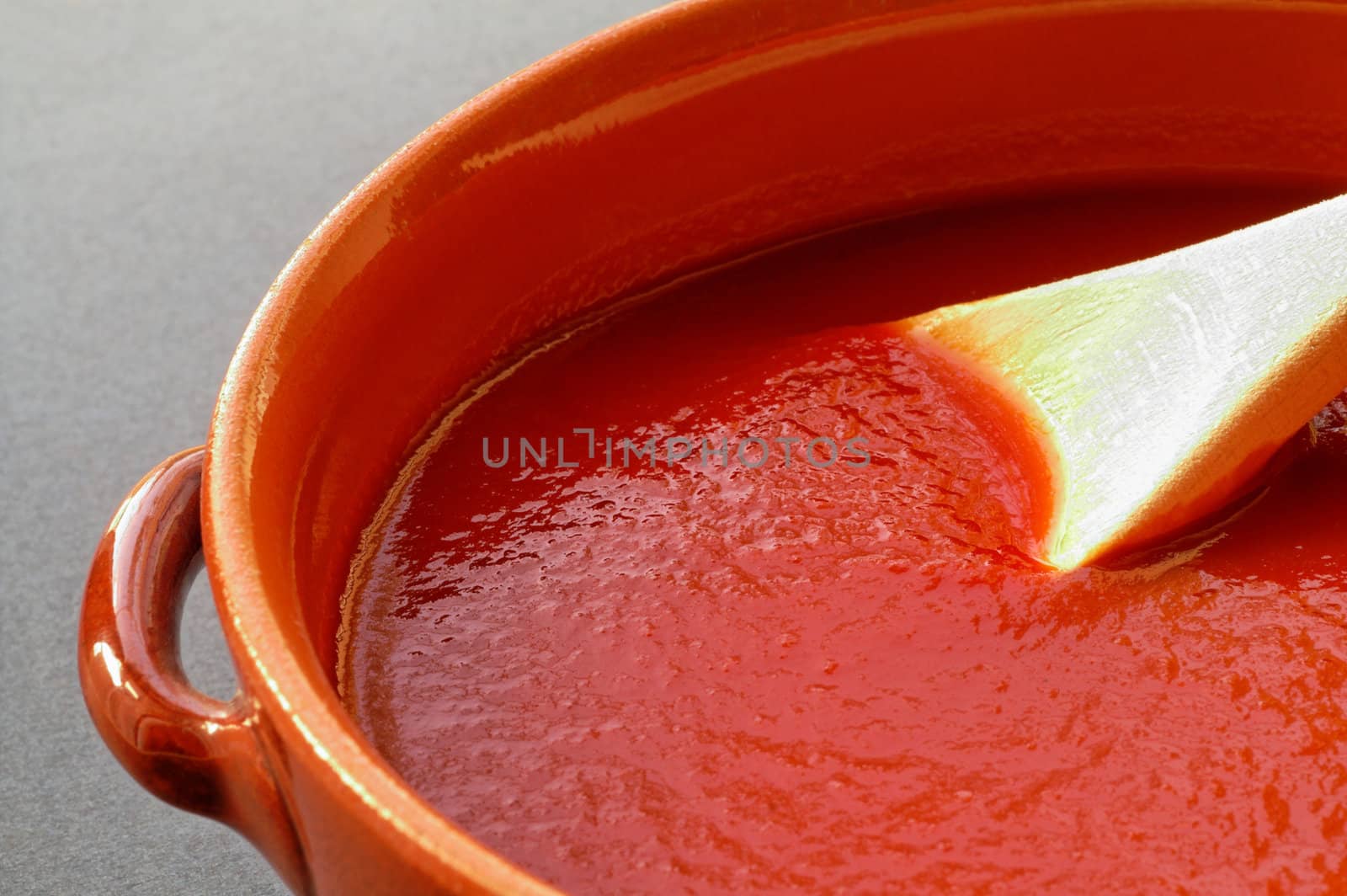 Terracotta pot and wooden spoon with tomato sauce. Closeup 1 by Laborer