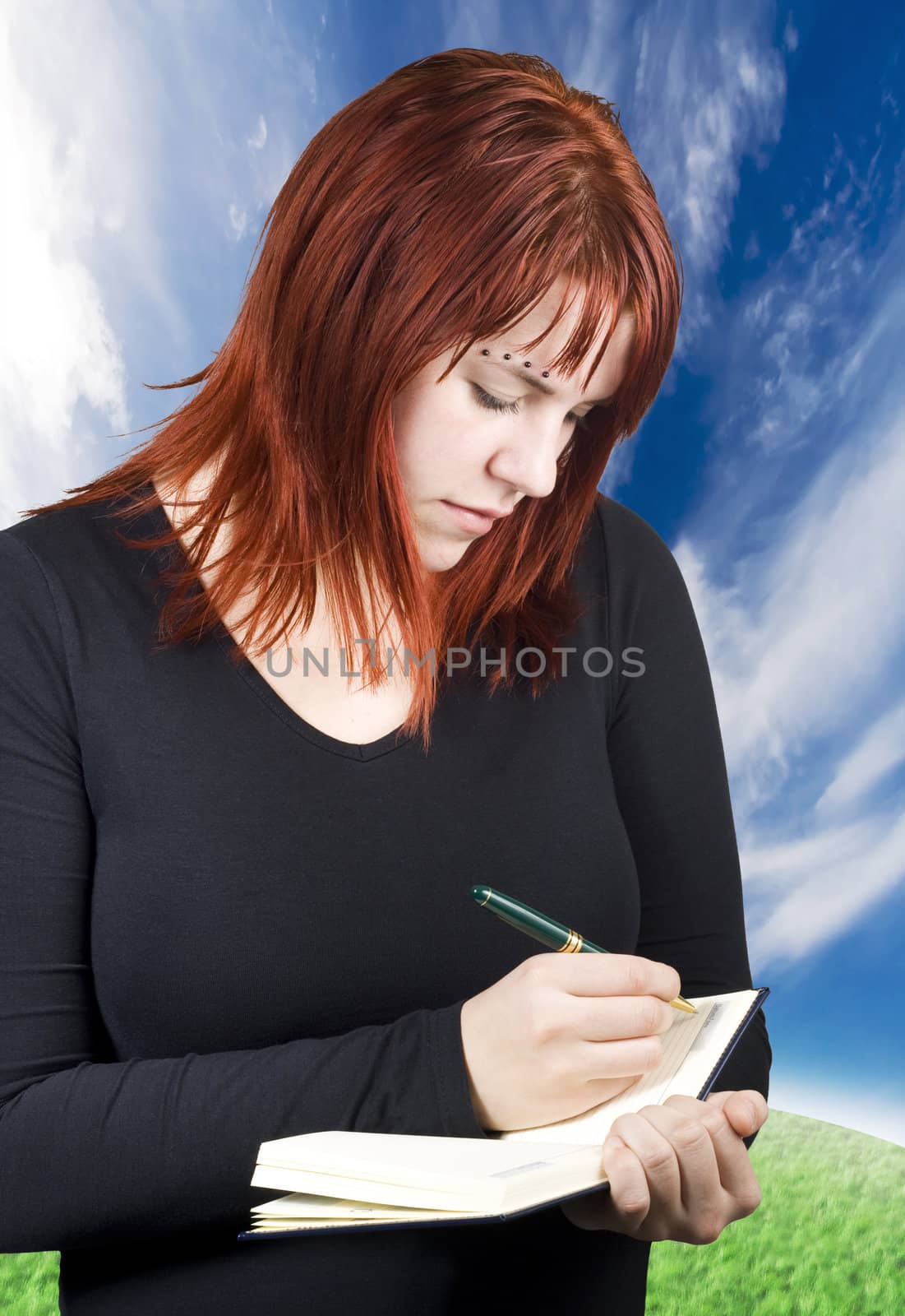 Cute girl with red hair writing in her diary or notebook with blank pages.