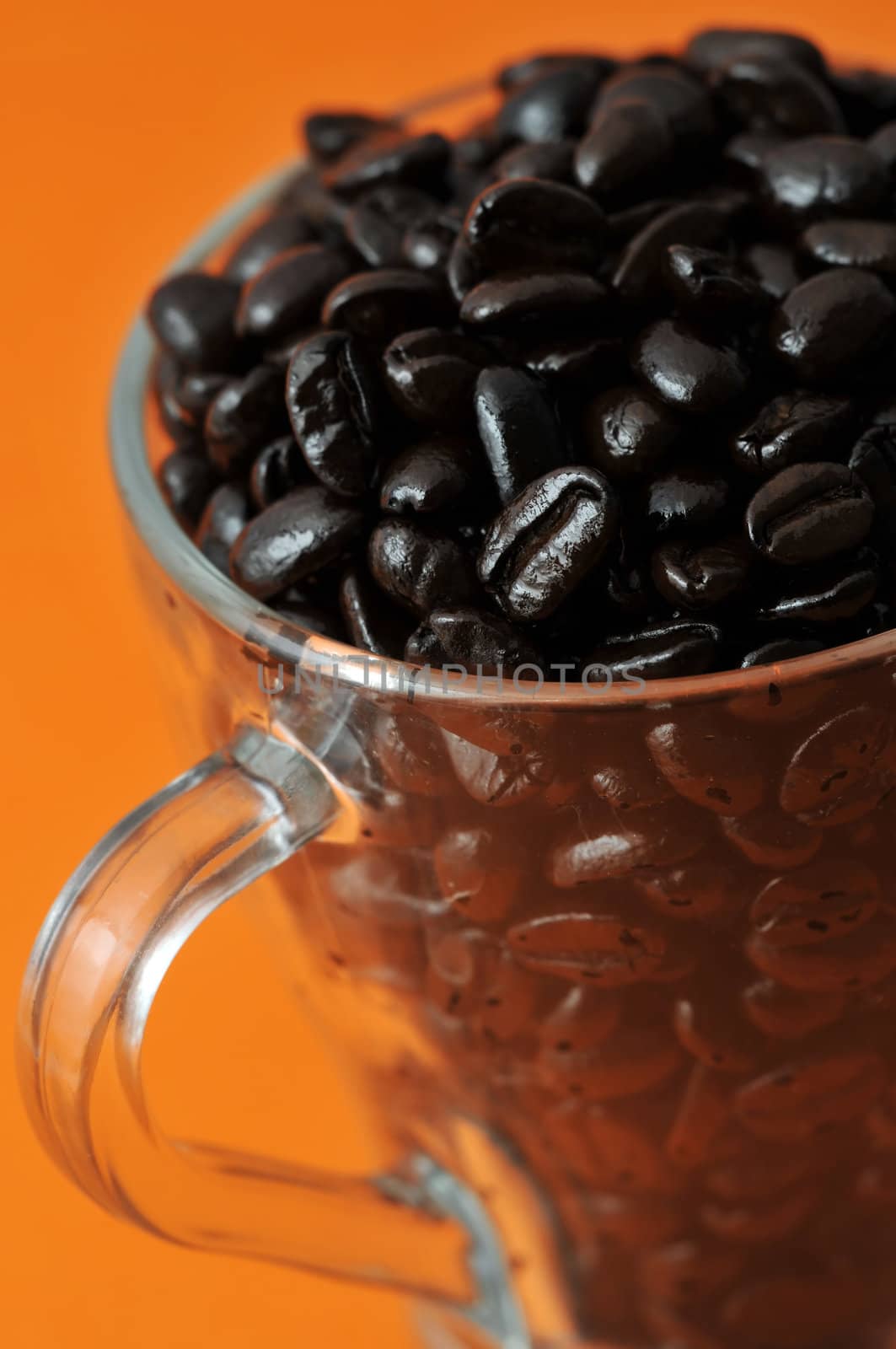 Transparent glass coffe cup with coffe beans isolated on orange