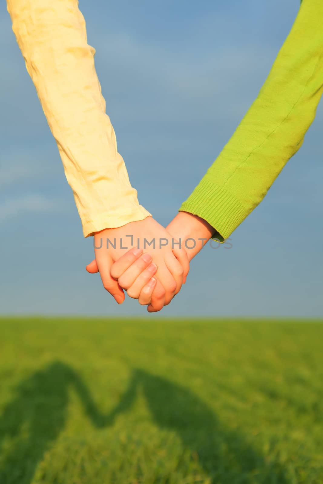 Teen girls holding hands against blue sky