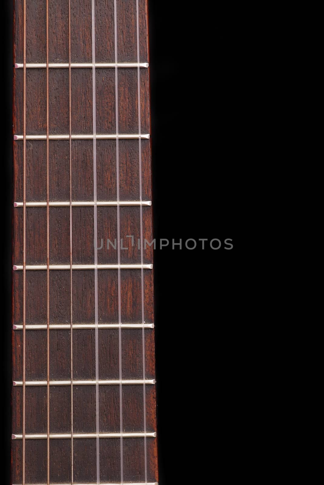 Detail of classic guitar (Spanish) fretboard, against black background.