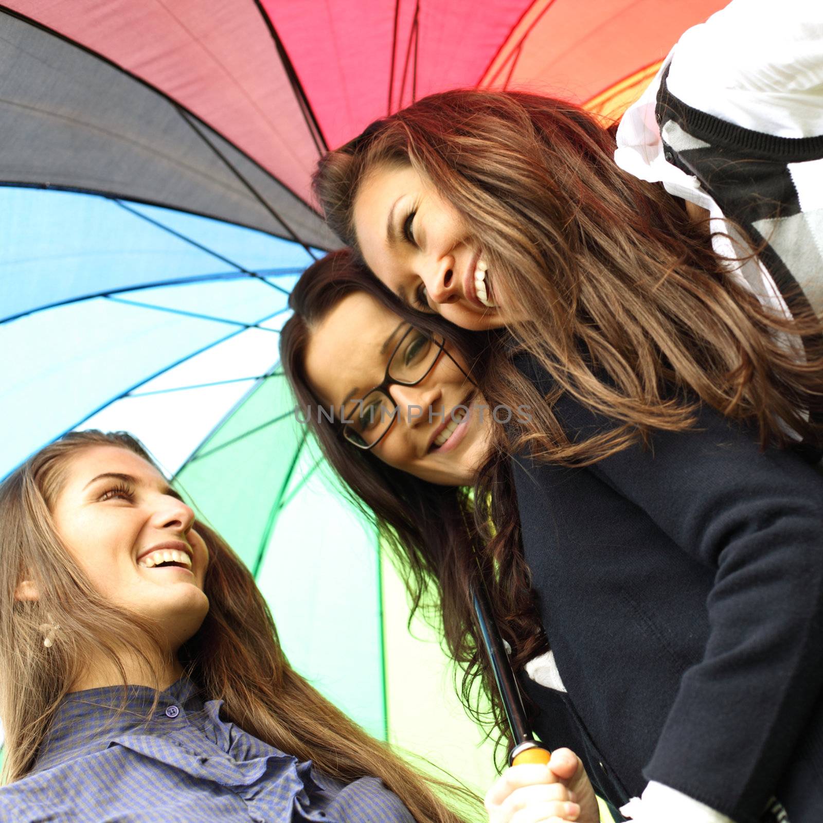 happy smiling girlfriends stay under colourful umbrella  