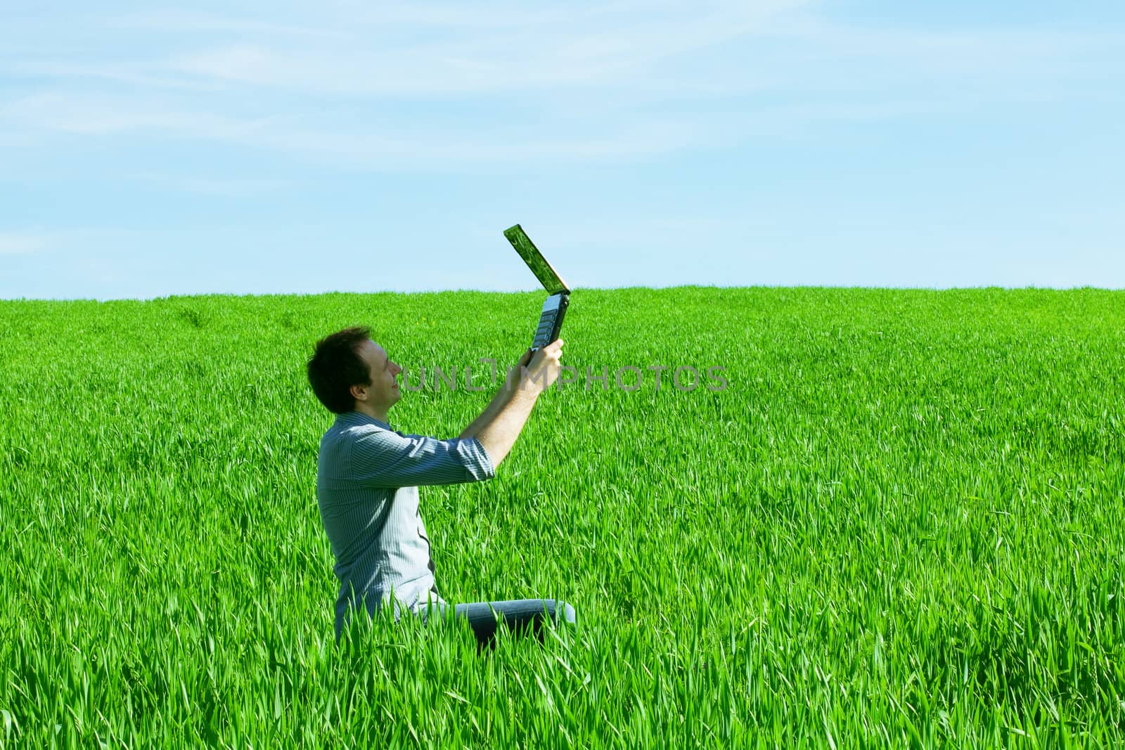 young man uses a laptop in the green field