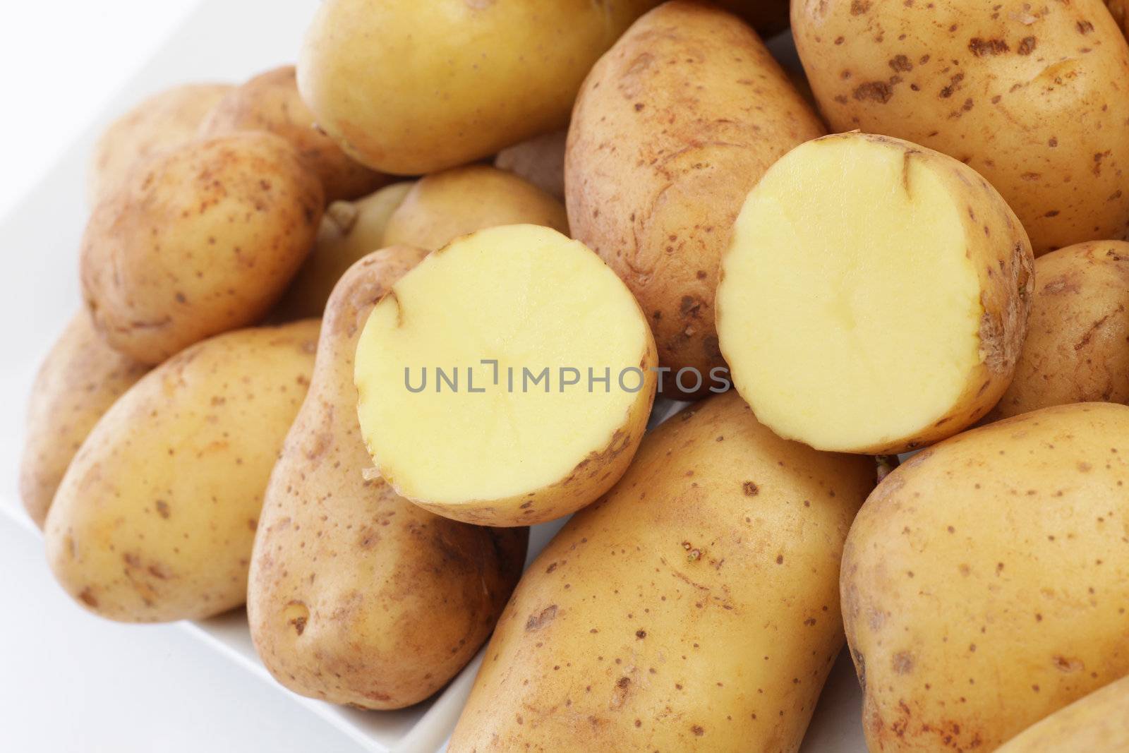 Closeup of a farmers market display of fresh whole potatoes with one cut through in half to show the firm flesh