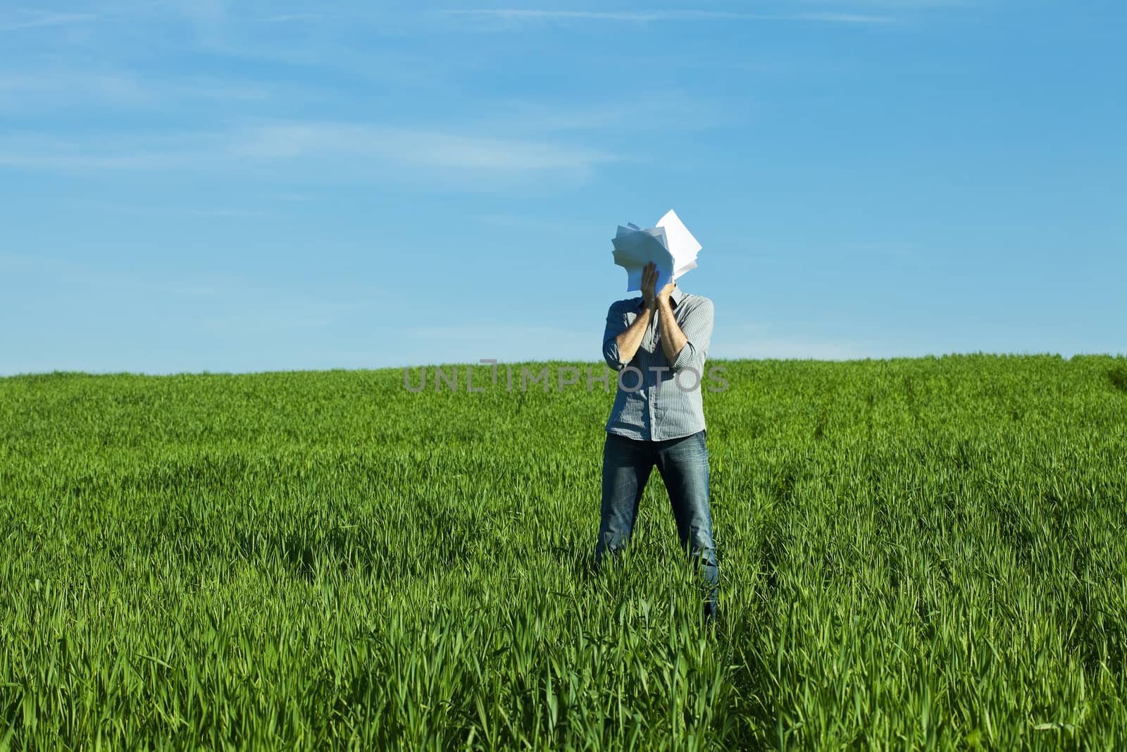 young man covering the face paper in green field