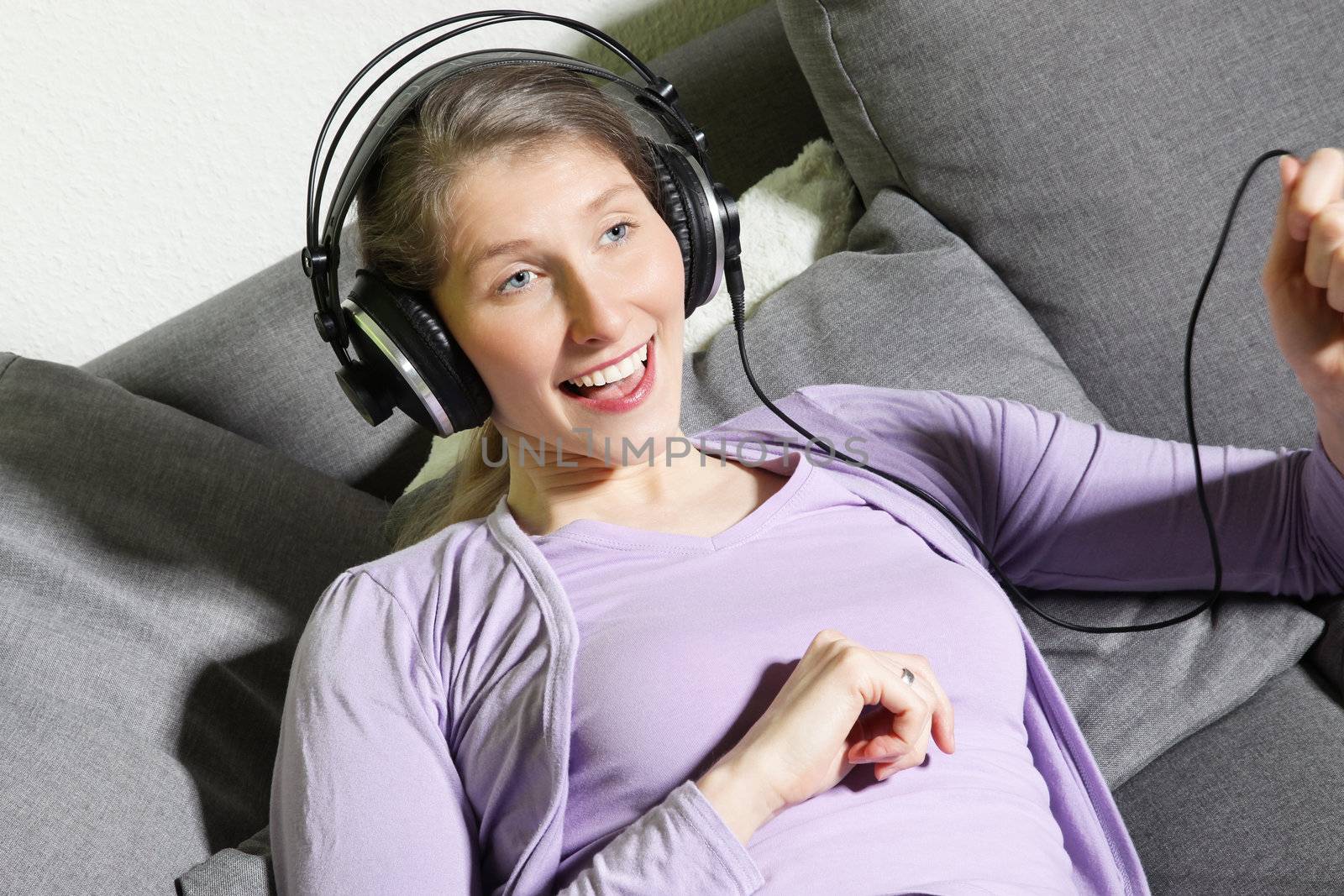Attractive vivacious middle-aged woman enjoying music and laughing as she follows the beat while sitting on a sofa in the living room