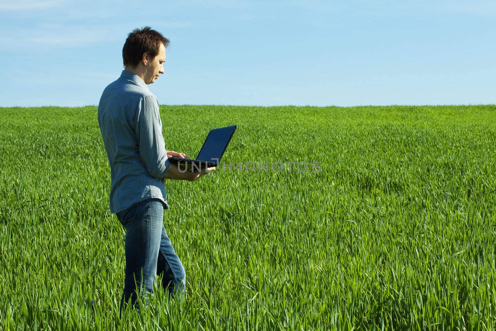 young man uses a laptop in the green field by jannyjus