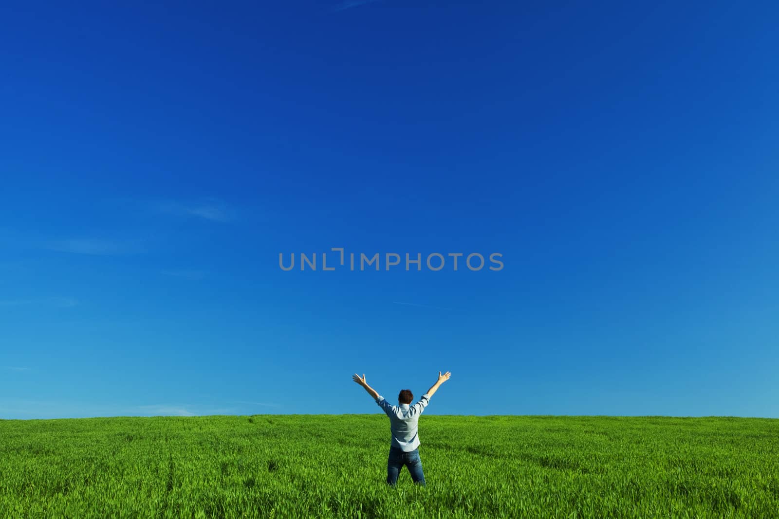 young man outstretched arms in green field against the blue sky by jannyjus