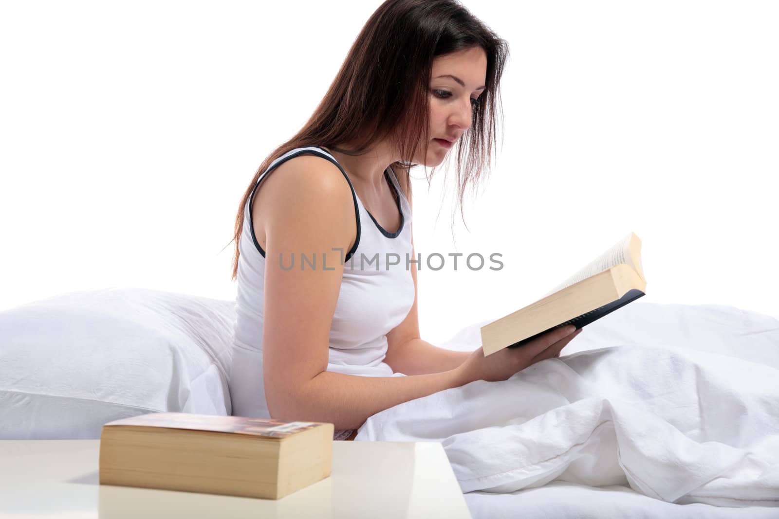 A young woman sitting on her bed reading a book. All on white background.