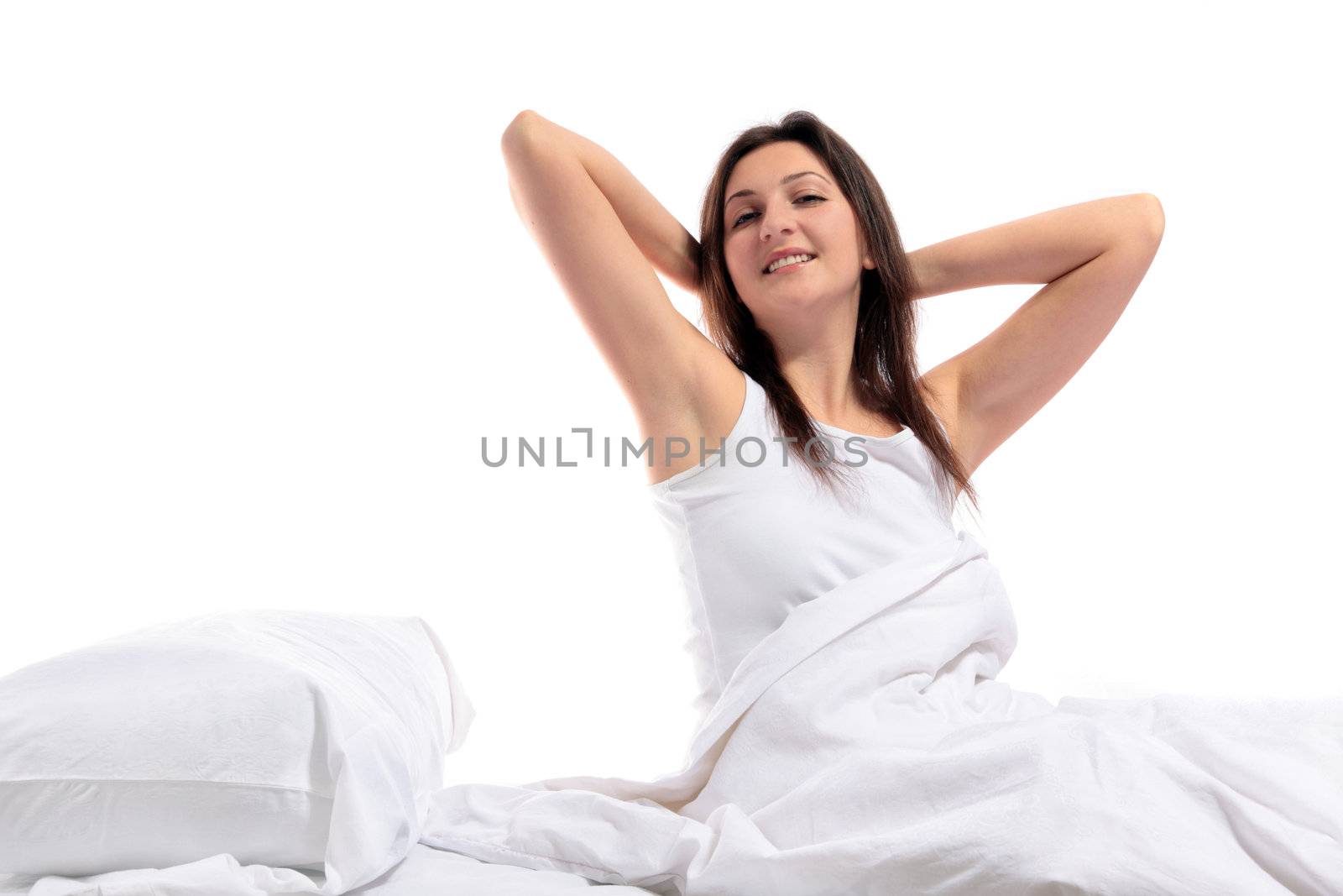 A well rested young woman sitting on her bed. All on white background.