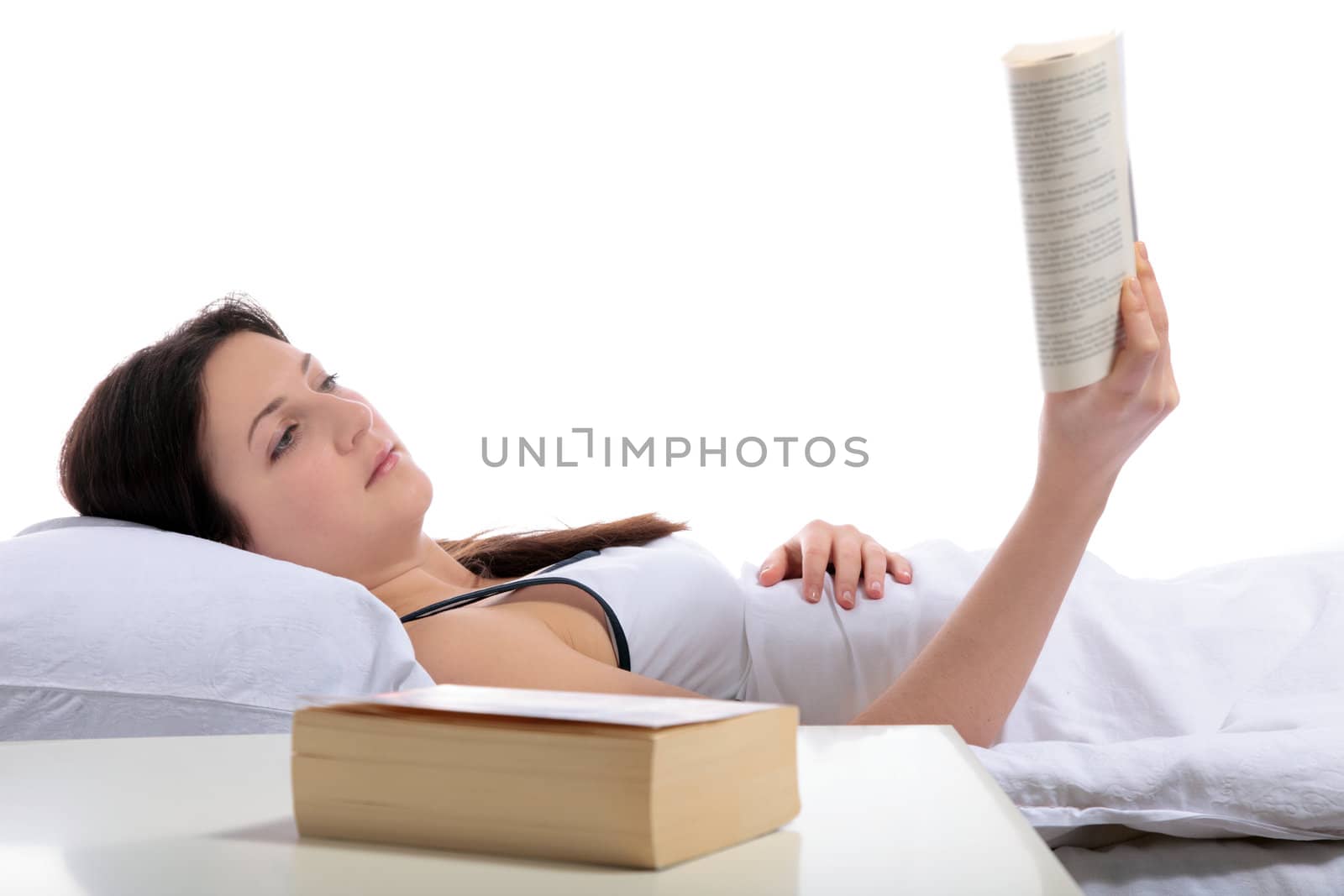 A young woman lying in her bed reading a book. All on white background.