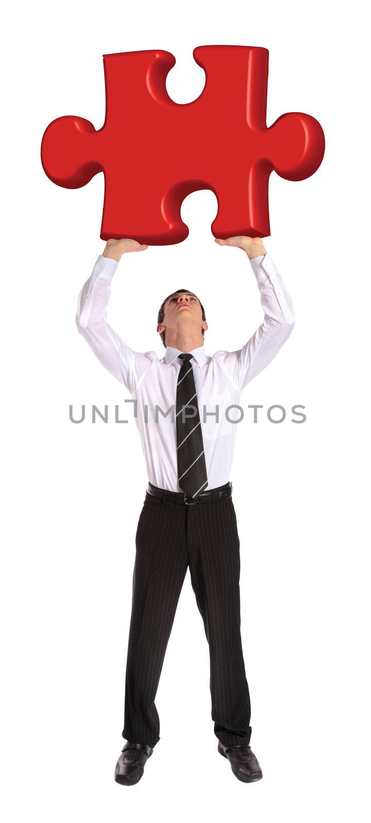 A young businessman stemming a huge piece of a puzzle. All on white background.