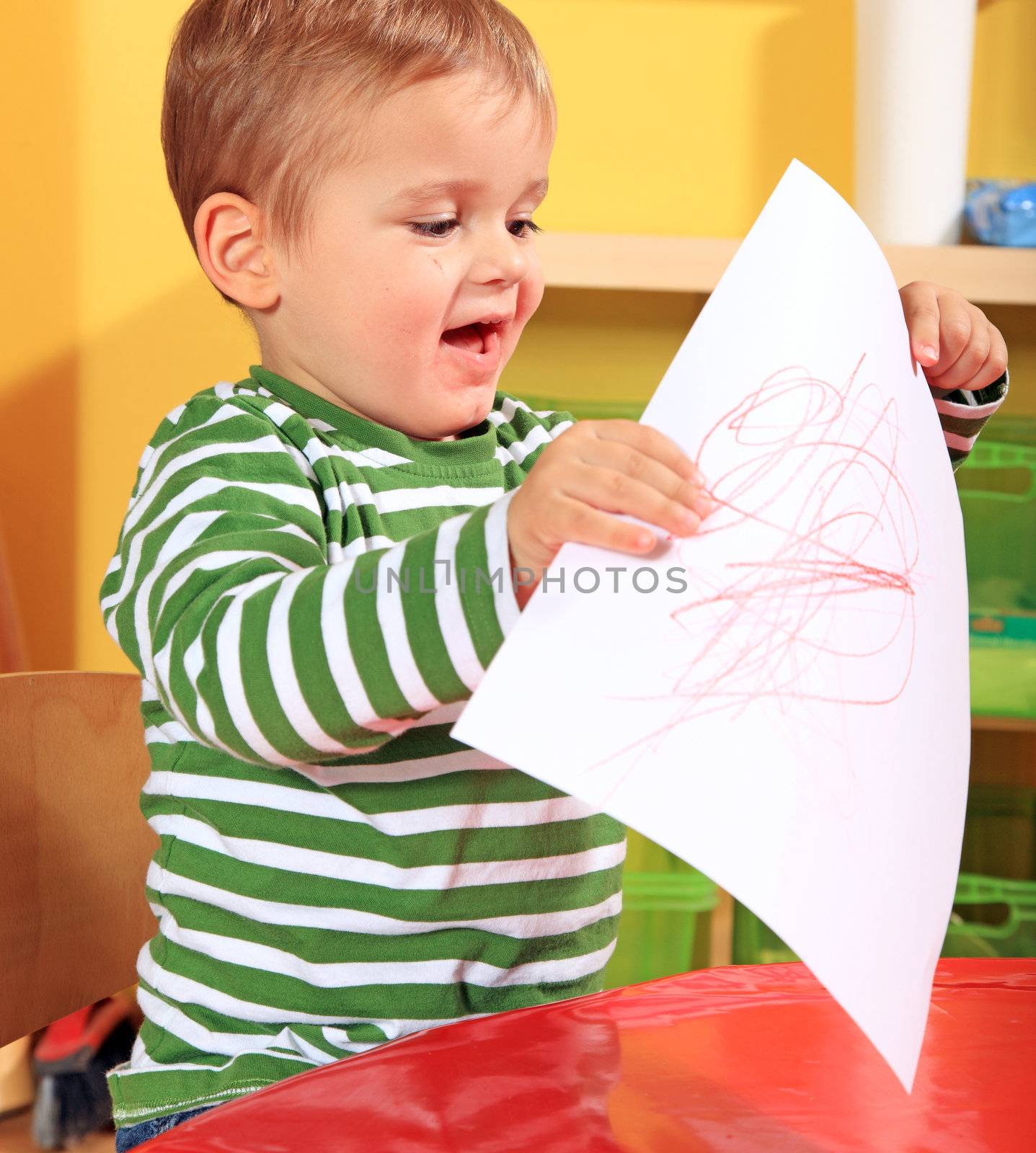 Cute caucasian toddler shows his drawn picture in kindergarten.