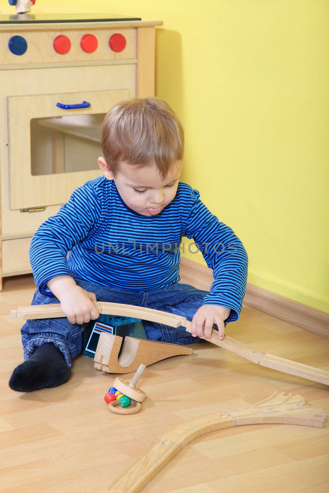 Cute european toddler playing with toy train in kindergarten.