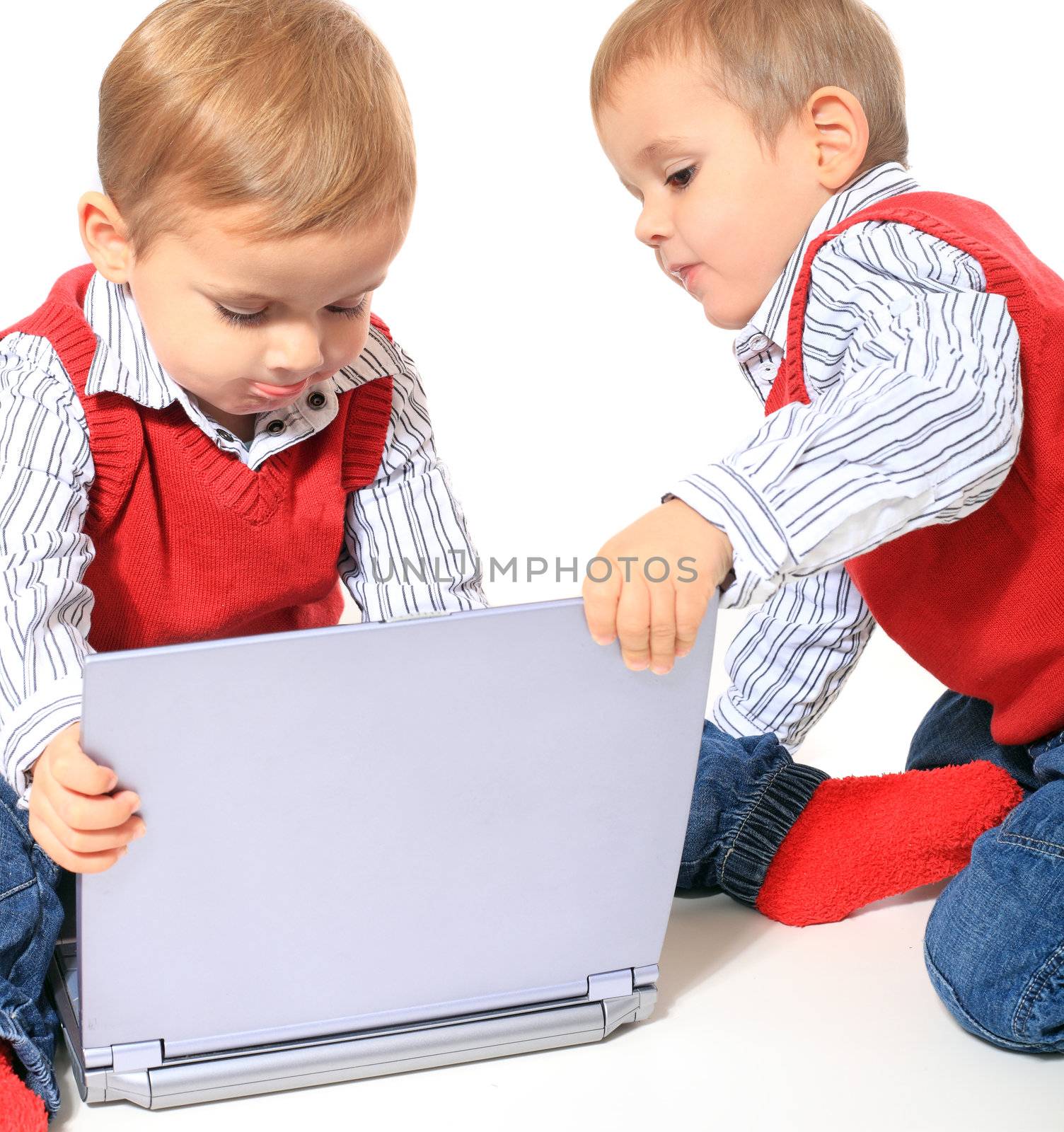 Cute caucasian twin brothers playing with notebook computer. All isolated on white background. Foreground in very light grey.