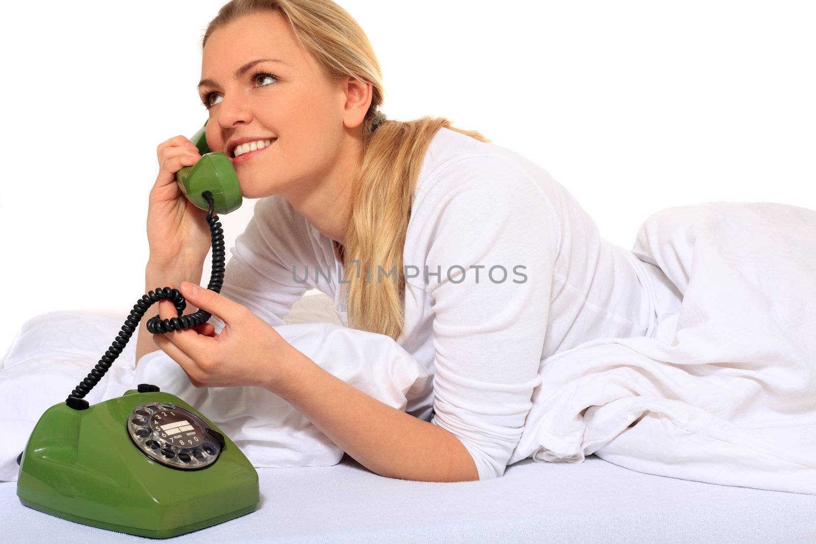 Attractive blond woman making a phone call while lying in bed. All on white background.