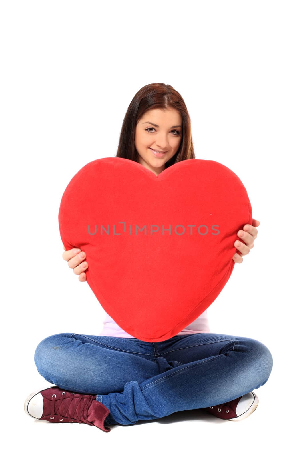 Attractive teenage girl holding heart-shaped red pillow. All on white background.