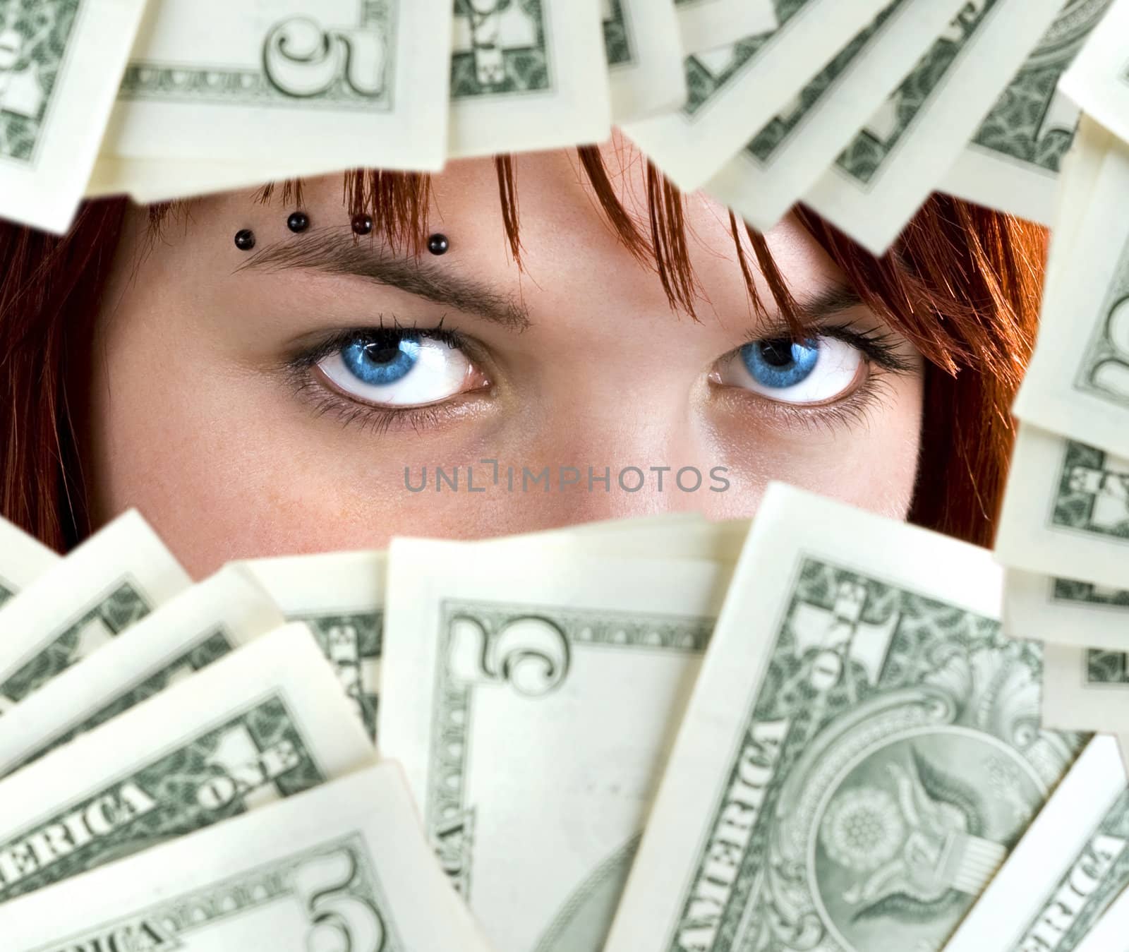 Piercing blue eyes of a cute redhead girl peeking through Dollar banknotes.