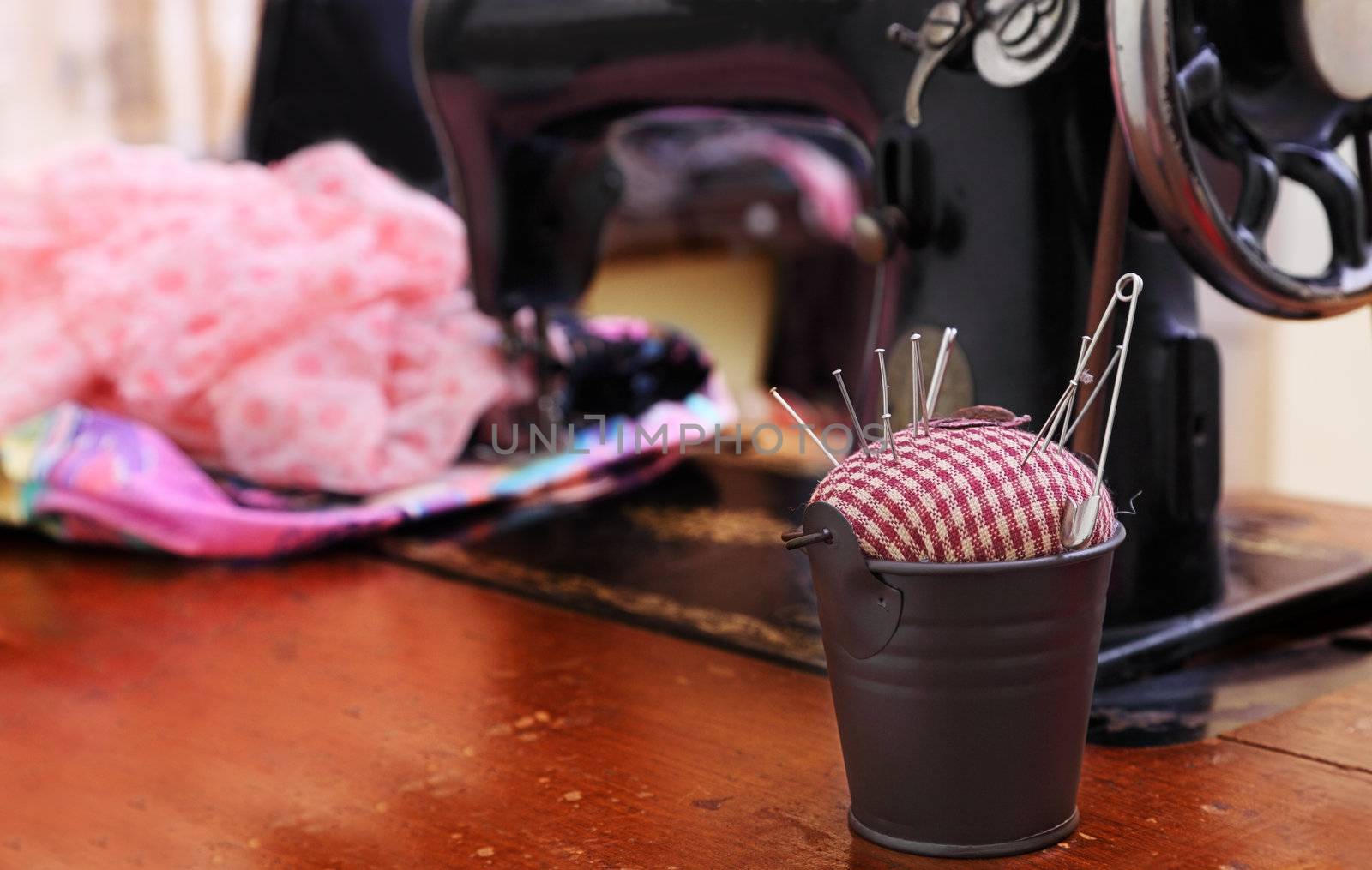 Image of an old-fashioned tailoring table.The selective focus is on the little pail with the pin-cushion.