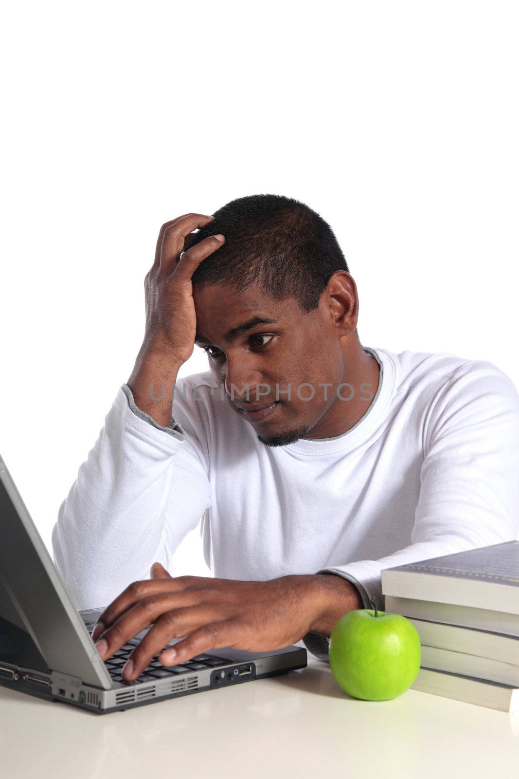 An attractive dark-skinned student in bad mood sitting in front of his notebook computer. All on white background.