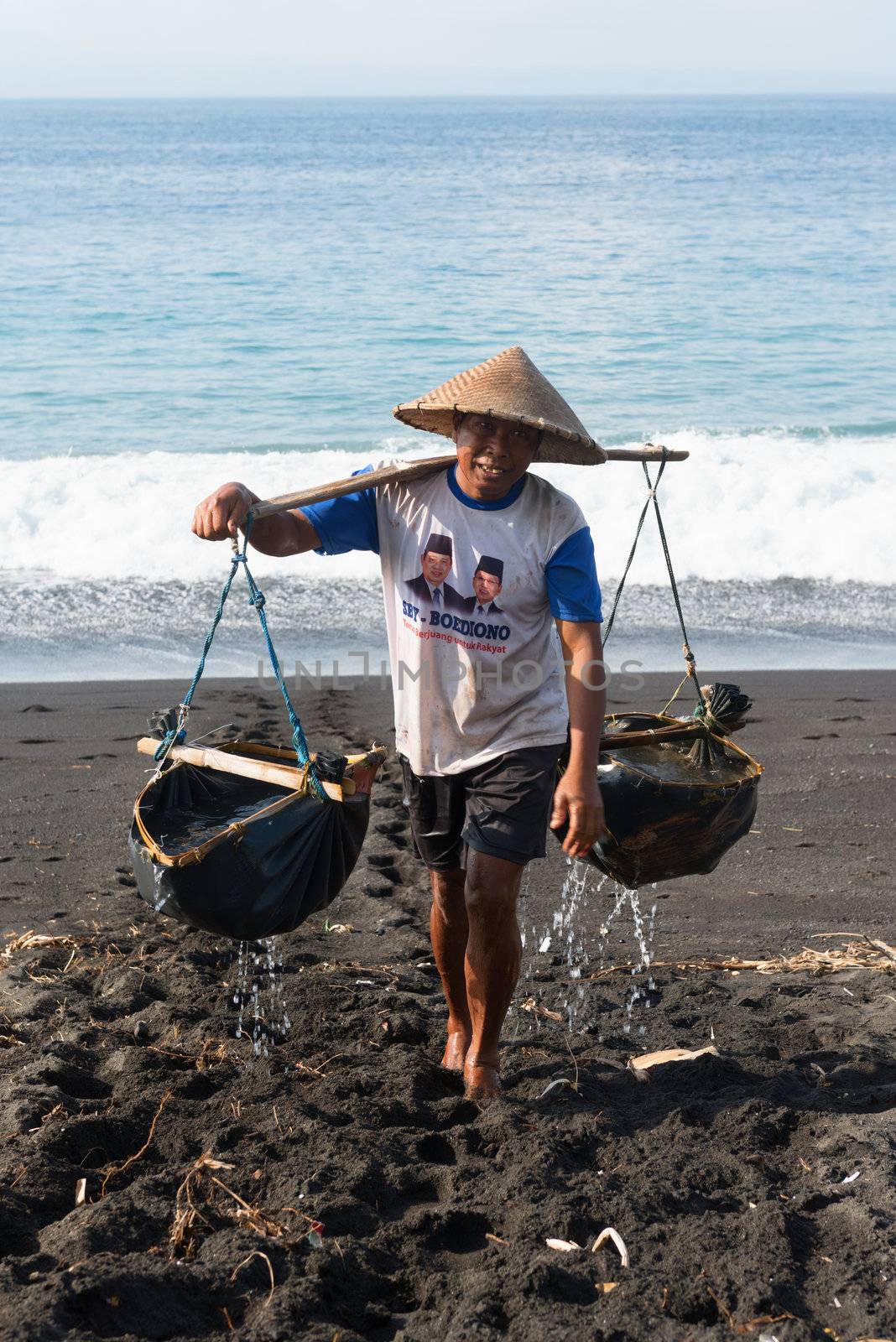 BALI, INDONESIA - SEP 26: Worker collects water for sea salt production on Sep 26, 2012 in Amuk Bay, Bali, Indonesia. It is unique tradition of salt production on volcanic black sand over 900 years. 