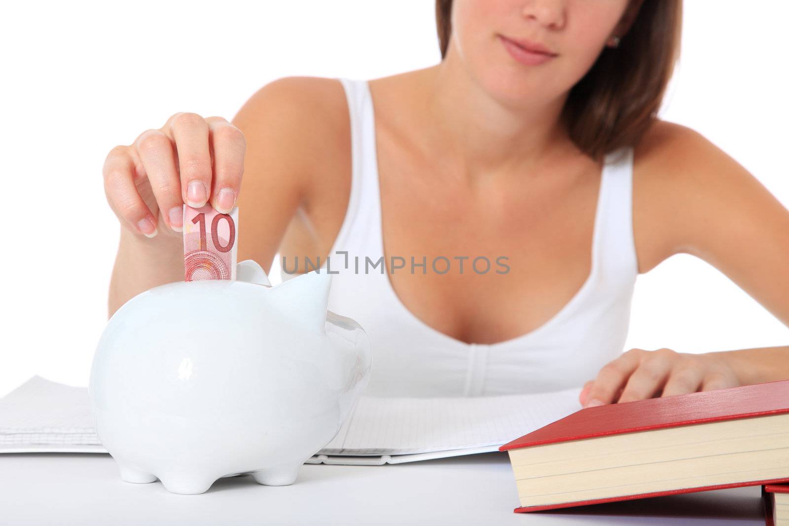 Attractive young student puts money in her piggy bank. All on white background.