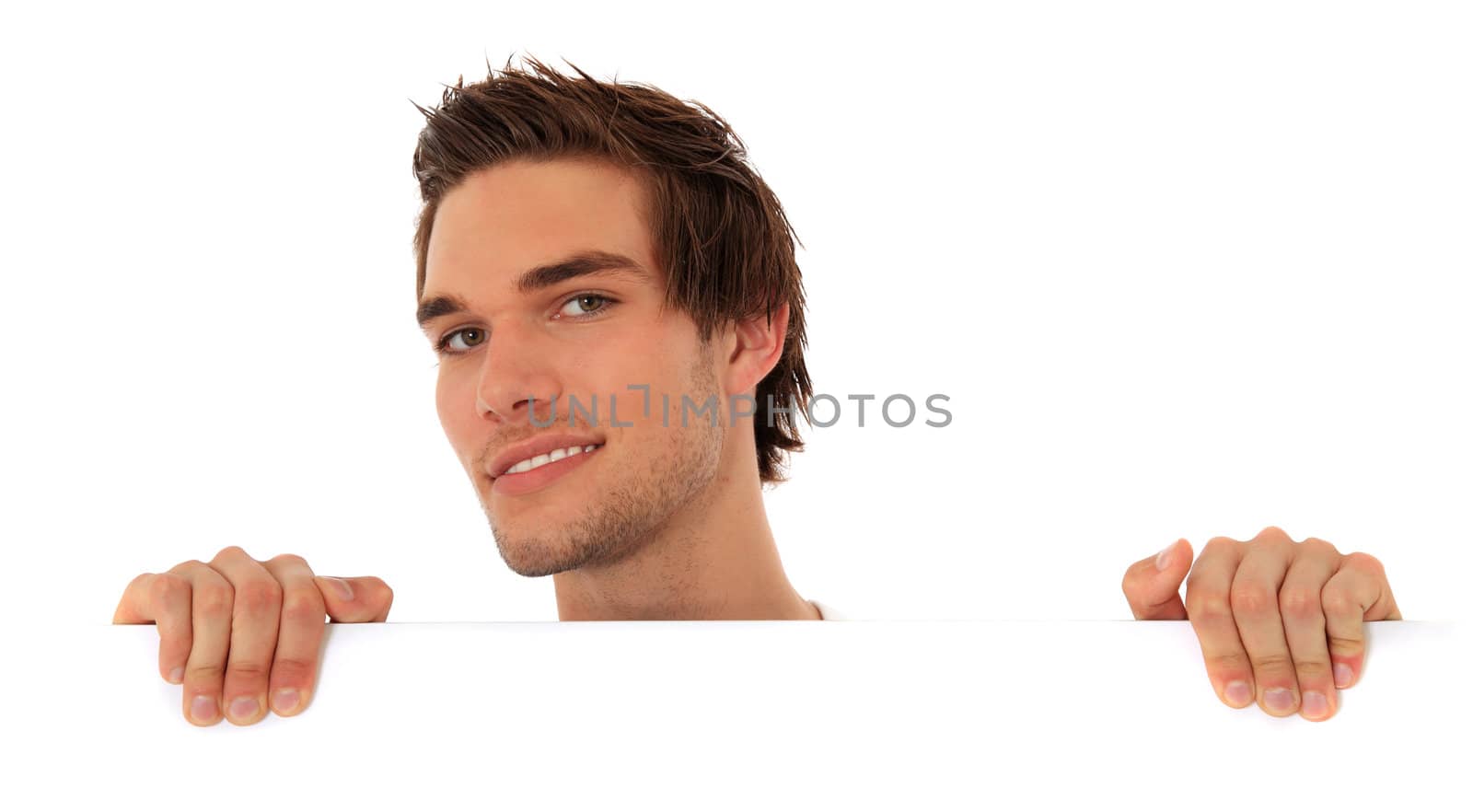 Attractive young man looking from behind a white wall. All on white background.