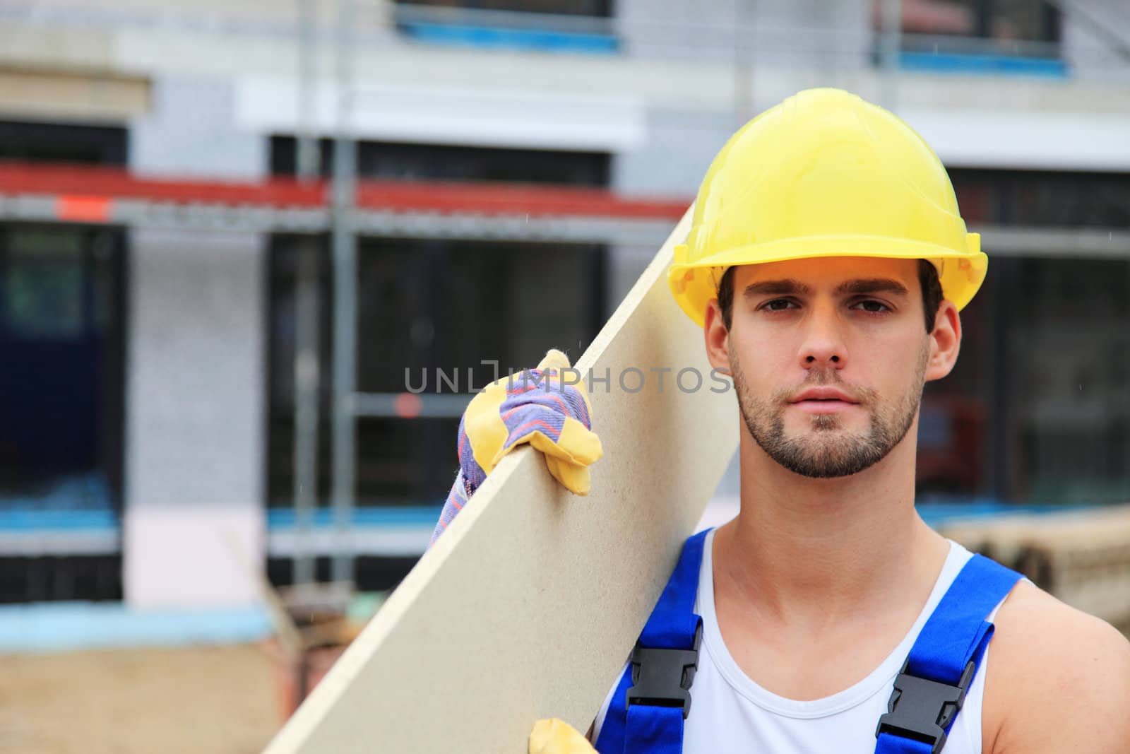 Manual worker on construction site carrying wooden board.