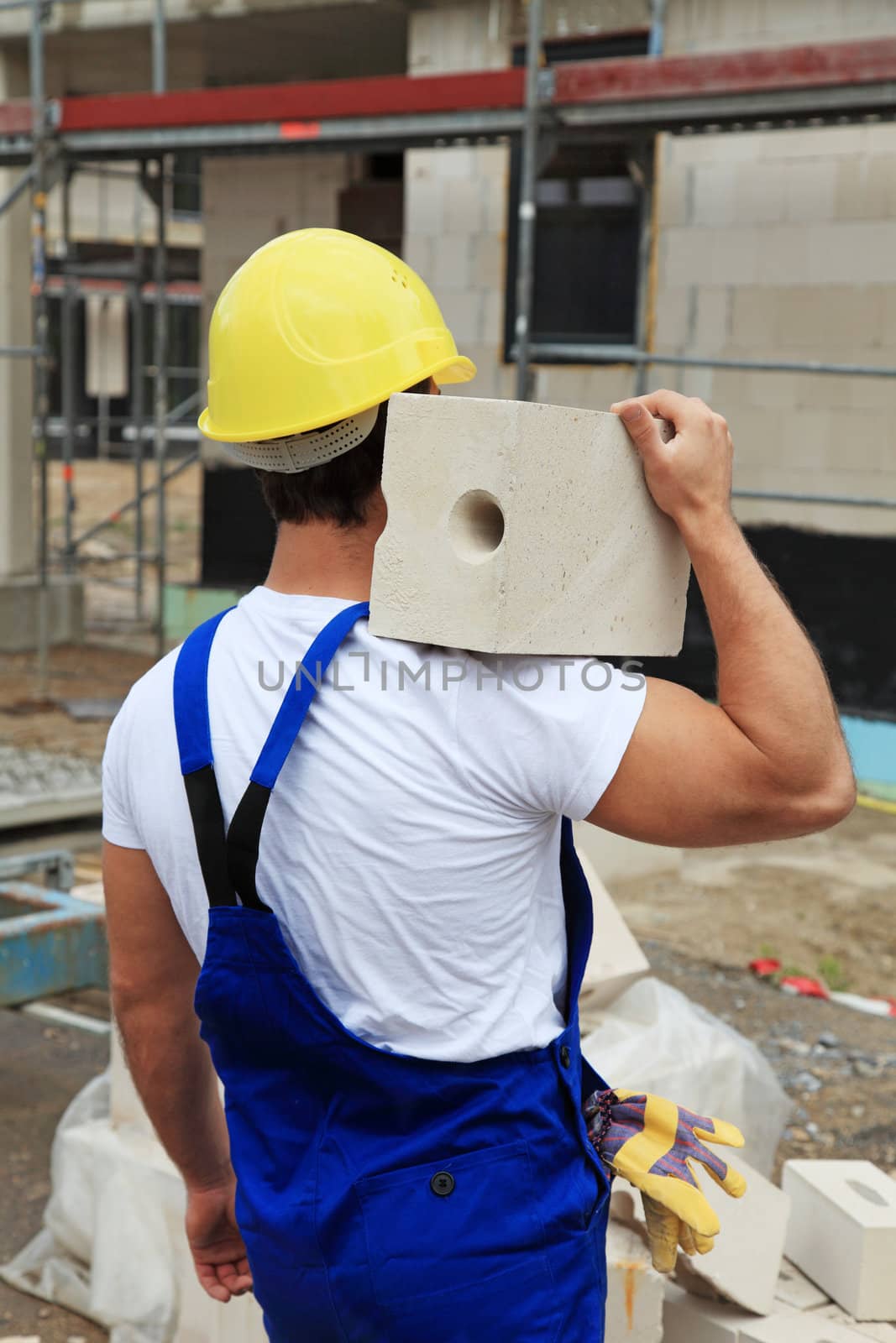 Manual worker on construction site carrying brick.