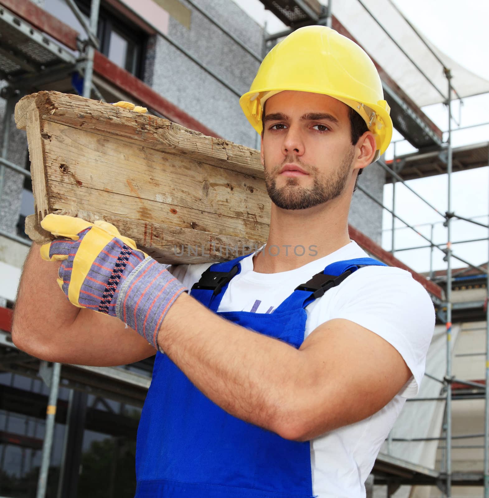 Manual worker on construction site carrying wooden board.