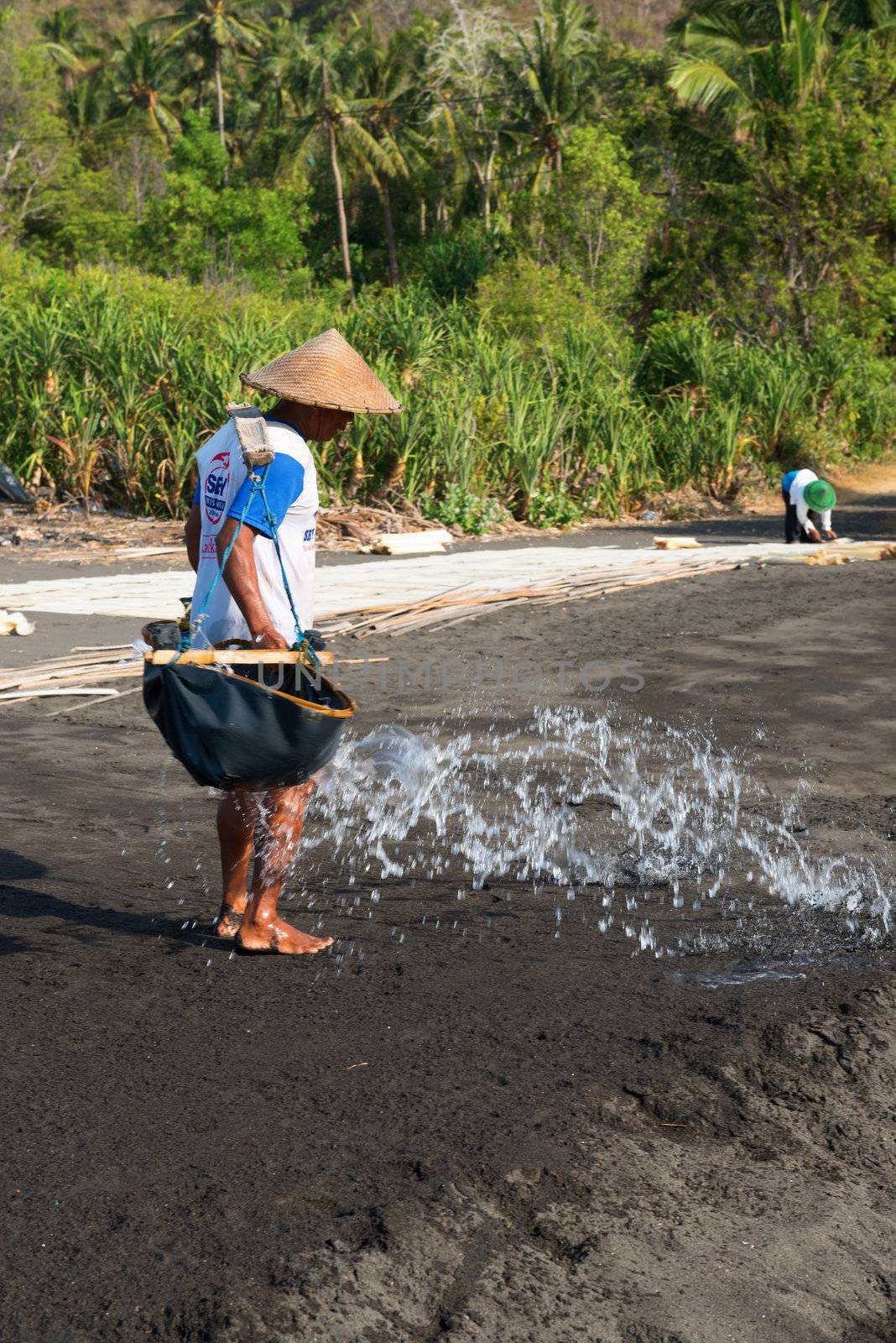 BALI, INDONESIA - SEP 26: Manual worker spreads sea water on black volcanic sand for salt production on Sep 26, 2012 in Amuk Bay, Bali, Indonesia. It is a unique tradition dating back over 900 years. 