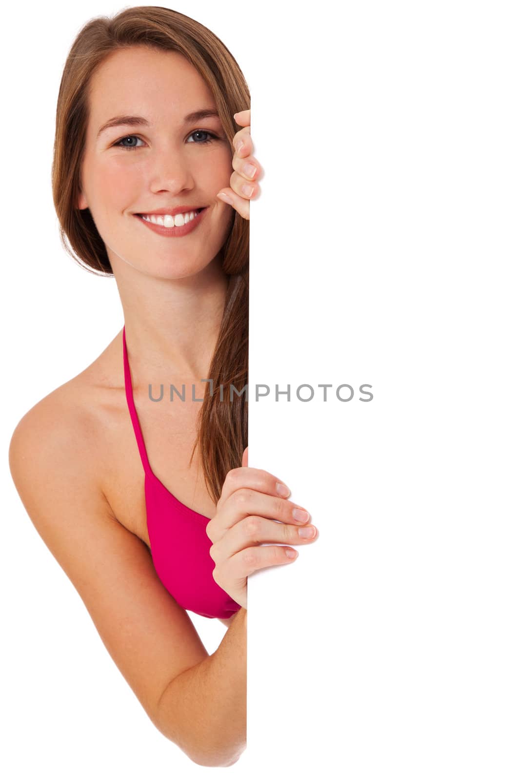 Attractive young woman in bikini standing behind white wall looking at blank sign. All on white background.