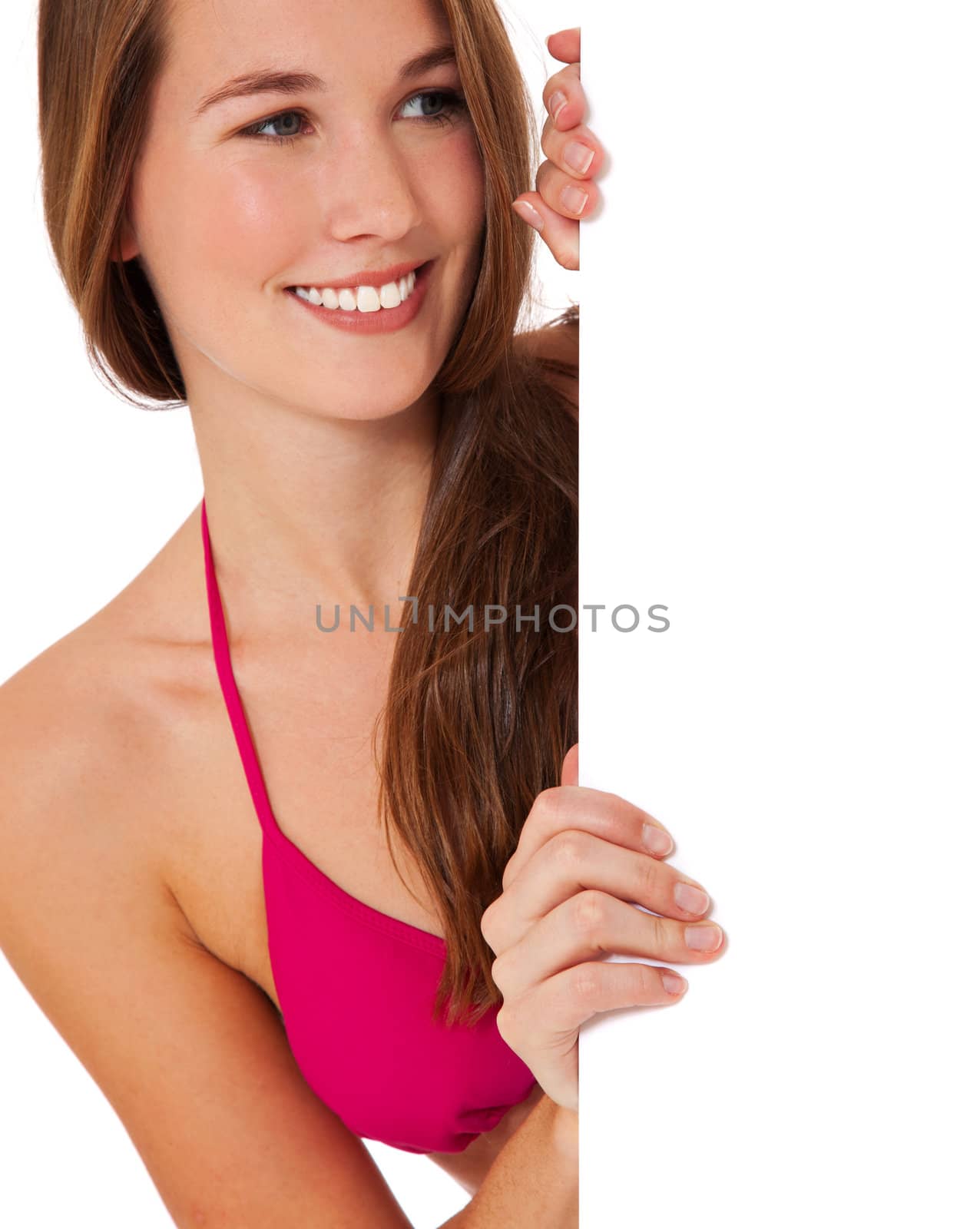 Attractive young woman in bikini standing behind white wall looking at blank sign. All on white background.