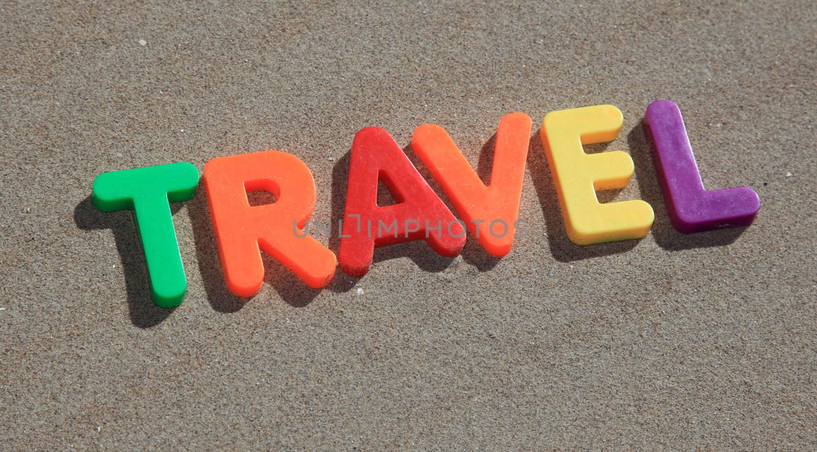 The term travel writtin in colorful letters on the sand.