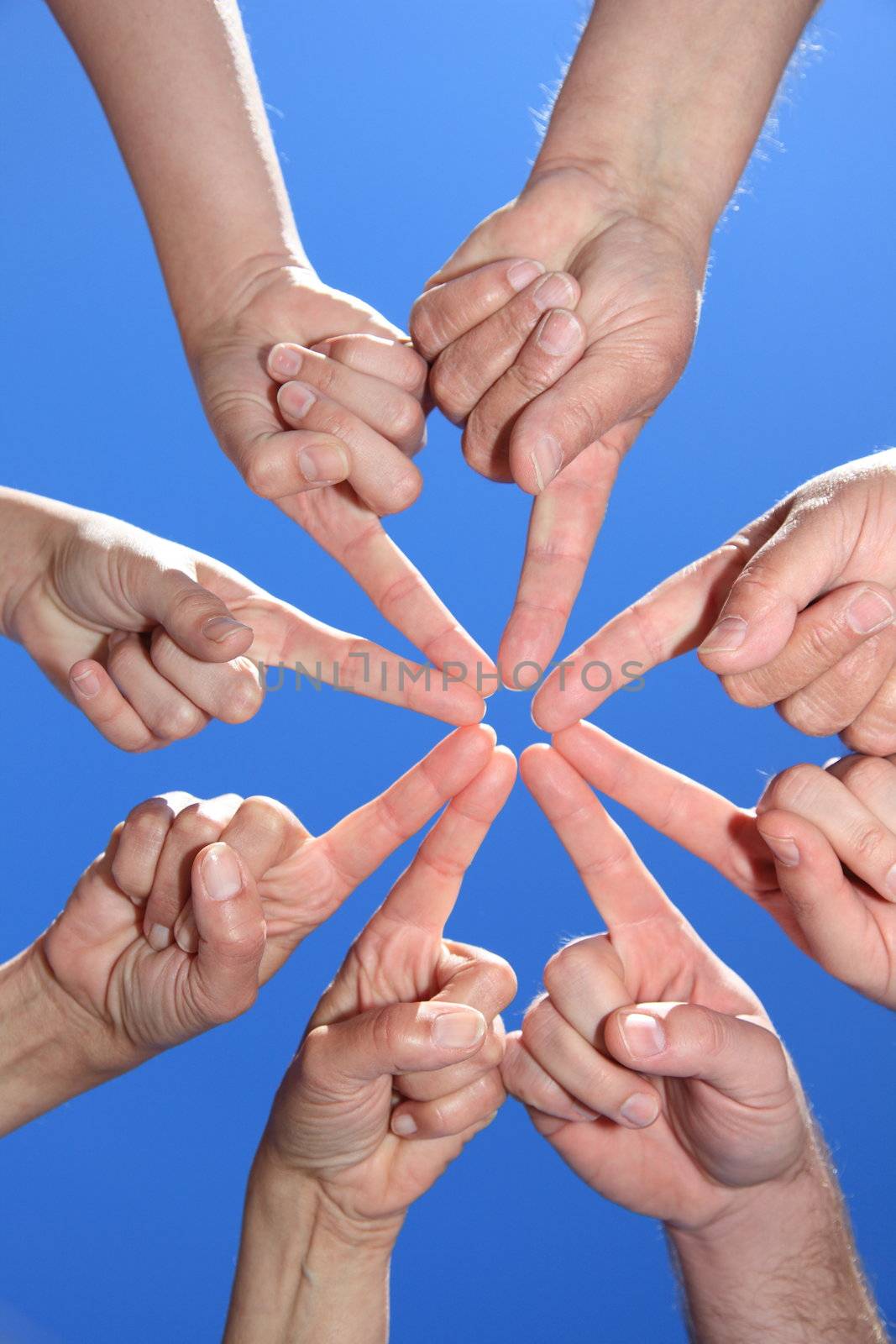 Various peoples hands in front of bright blue sky forming a star.