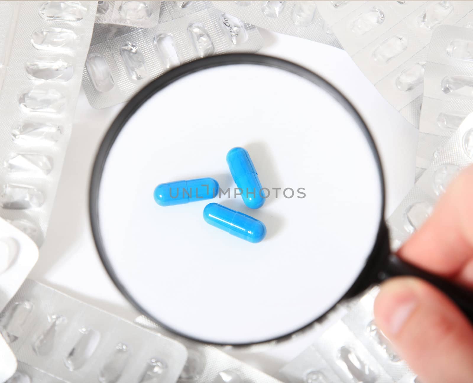 Conceptual shot of a person checking pharmaceuticals with magnifier. All on white background.