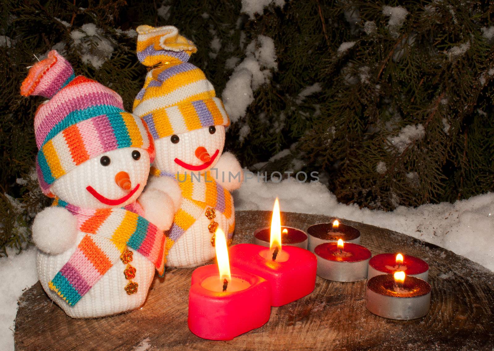Two snowmen with two burning heart shaped candles staying outdoors