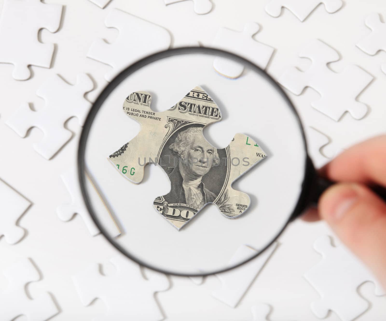 Person using magnifier to check piece of puzzle with topic of a dollar note.