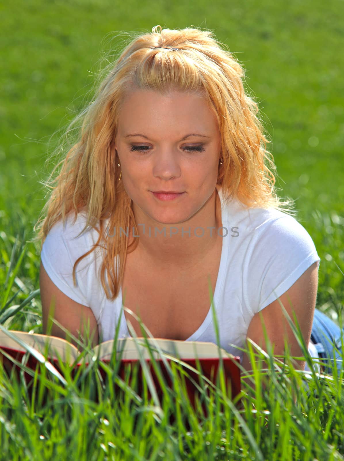 Attractive young woman resting outside on green meadow, reading a book.