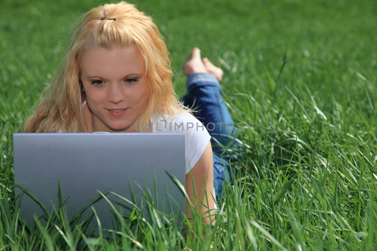 Attractive young woman resting outside on green meadow using laptop.