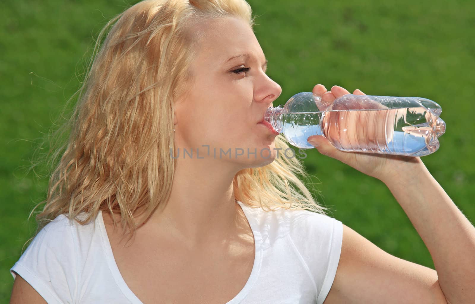 Attractive young woman resting outside on green meadow having a drink.