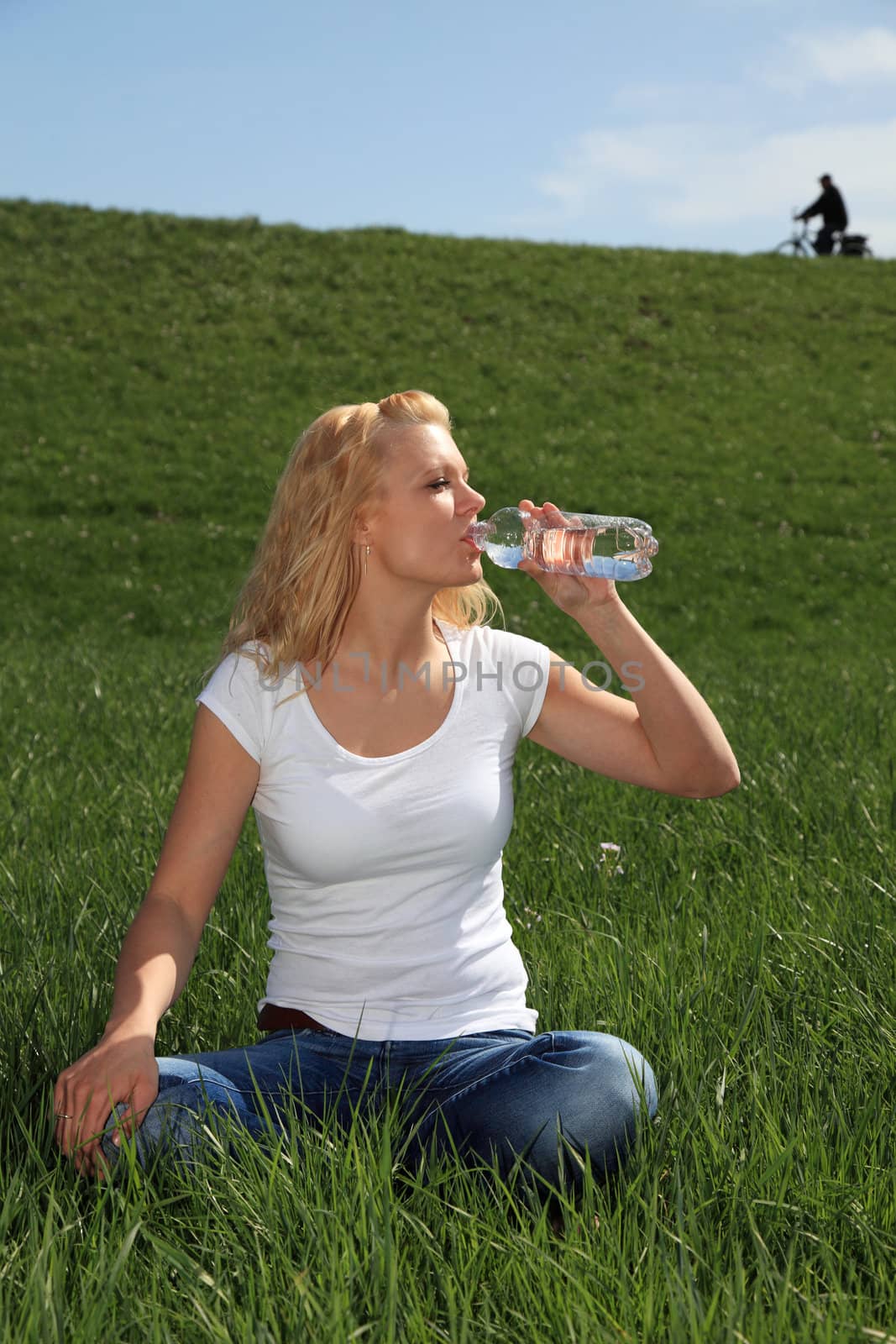 Attractive young woman resting outside on green meadow having a drink.