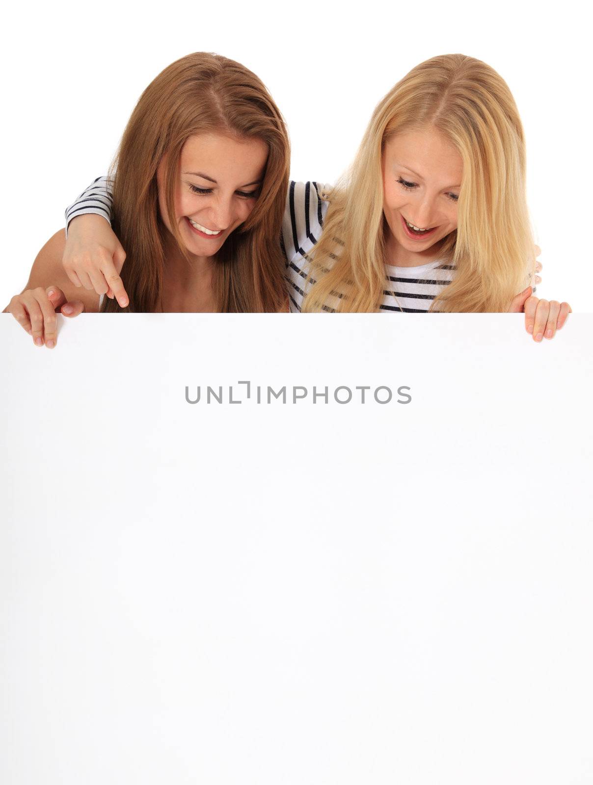 Two happy young women looking down a blank white sign with plenty copy space. All on white background.
