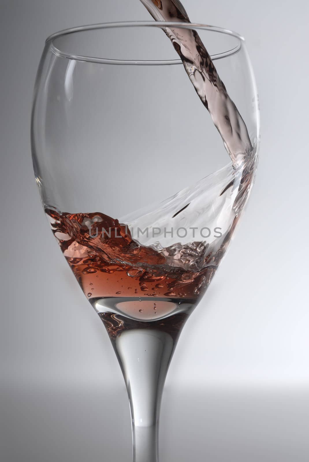 Rose wine being poured into a clean wine glass against a grey backround.