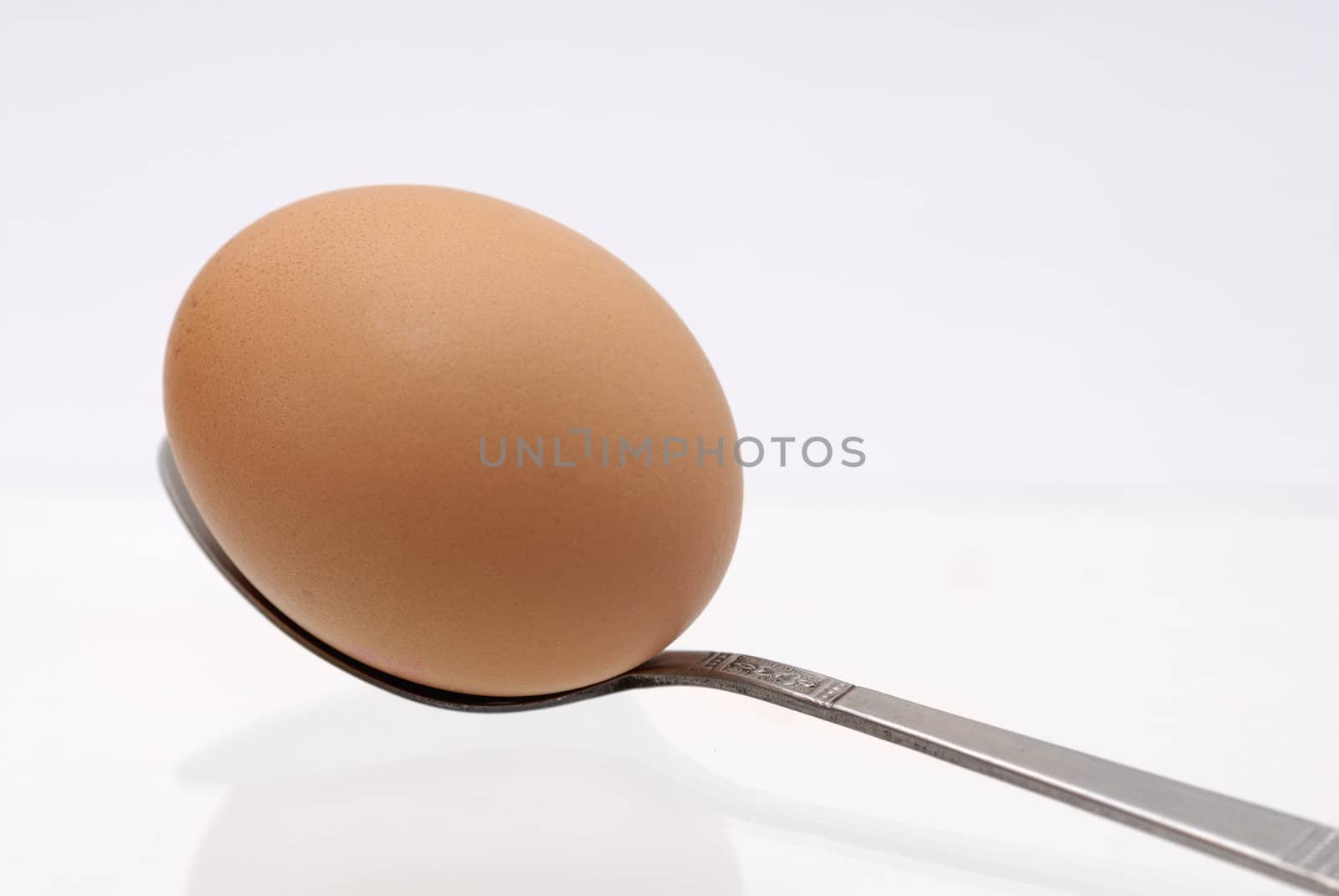 One egg balancing on a teaspoon against white background.