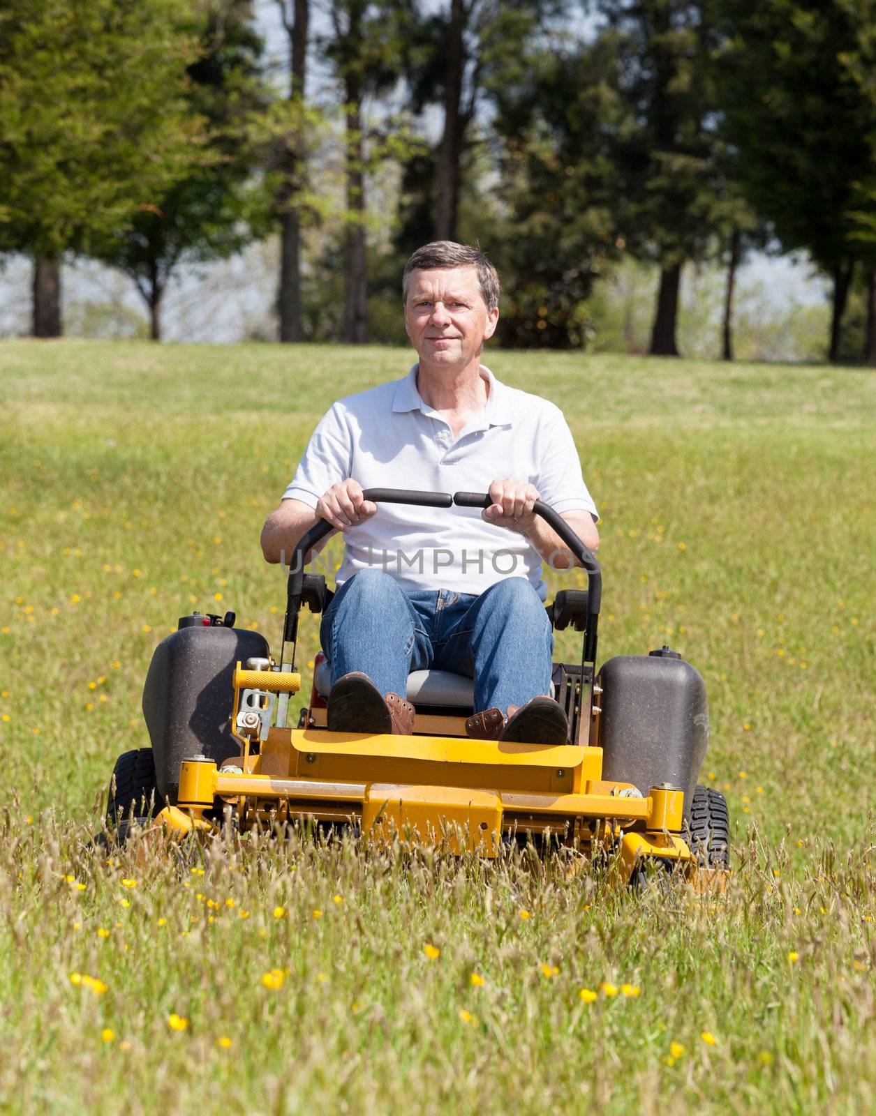 Senior retired male cutting the grass on expansive lawn using yellow zero-turn mower
