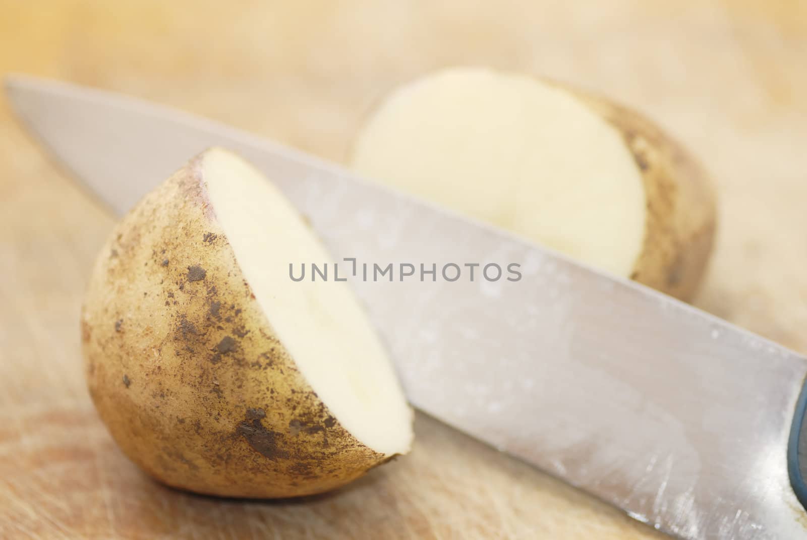 One Kestrel potato cut in half on chopping board. Focus on first half.