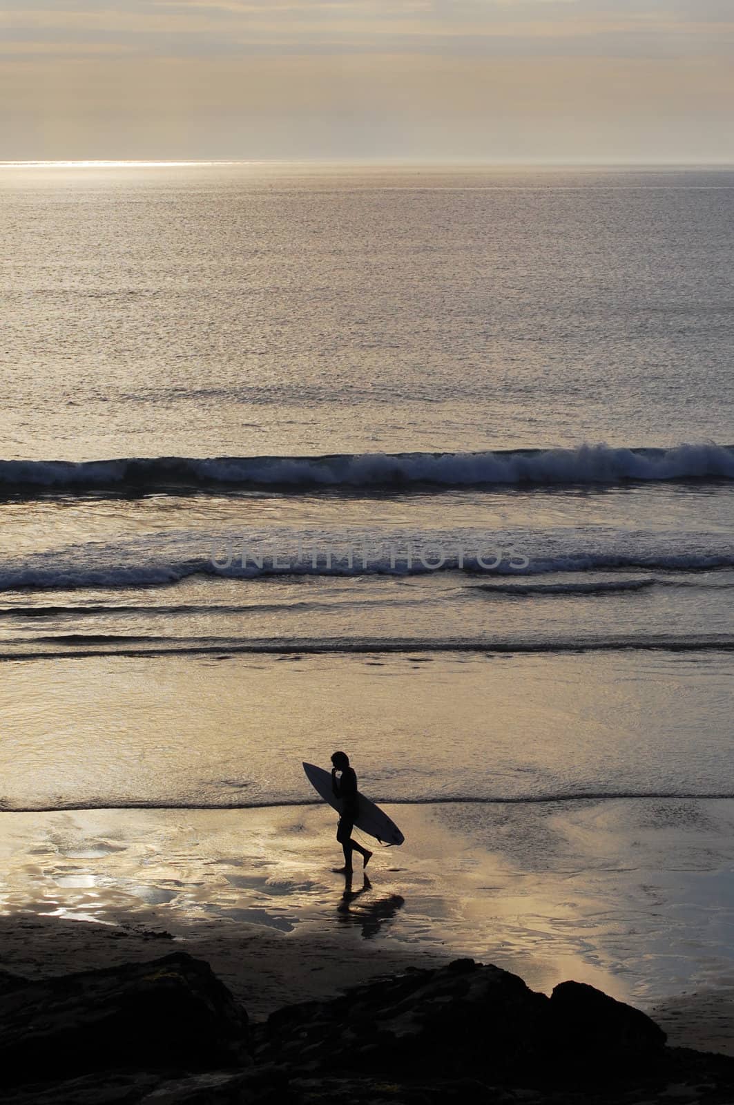 Surfer walking accross the beach at sunset. Trebarwith Strand, Cornwall, UK.