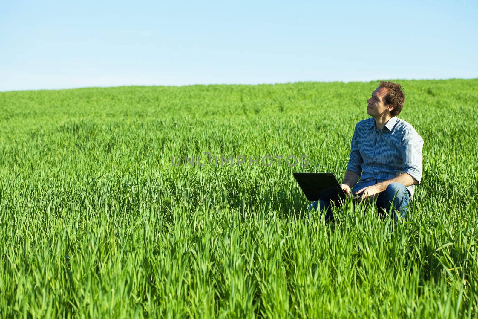 young man using laptop in the field by jannyjus